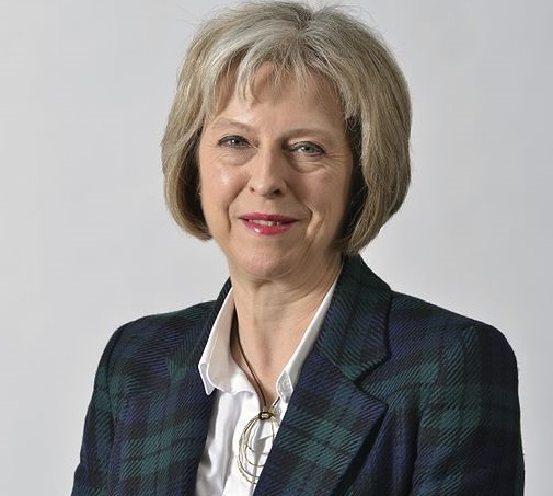 Theresa May i rutig kavaj ler.