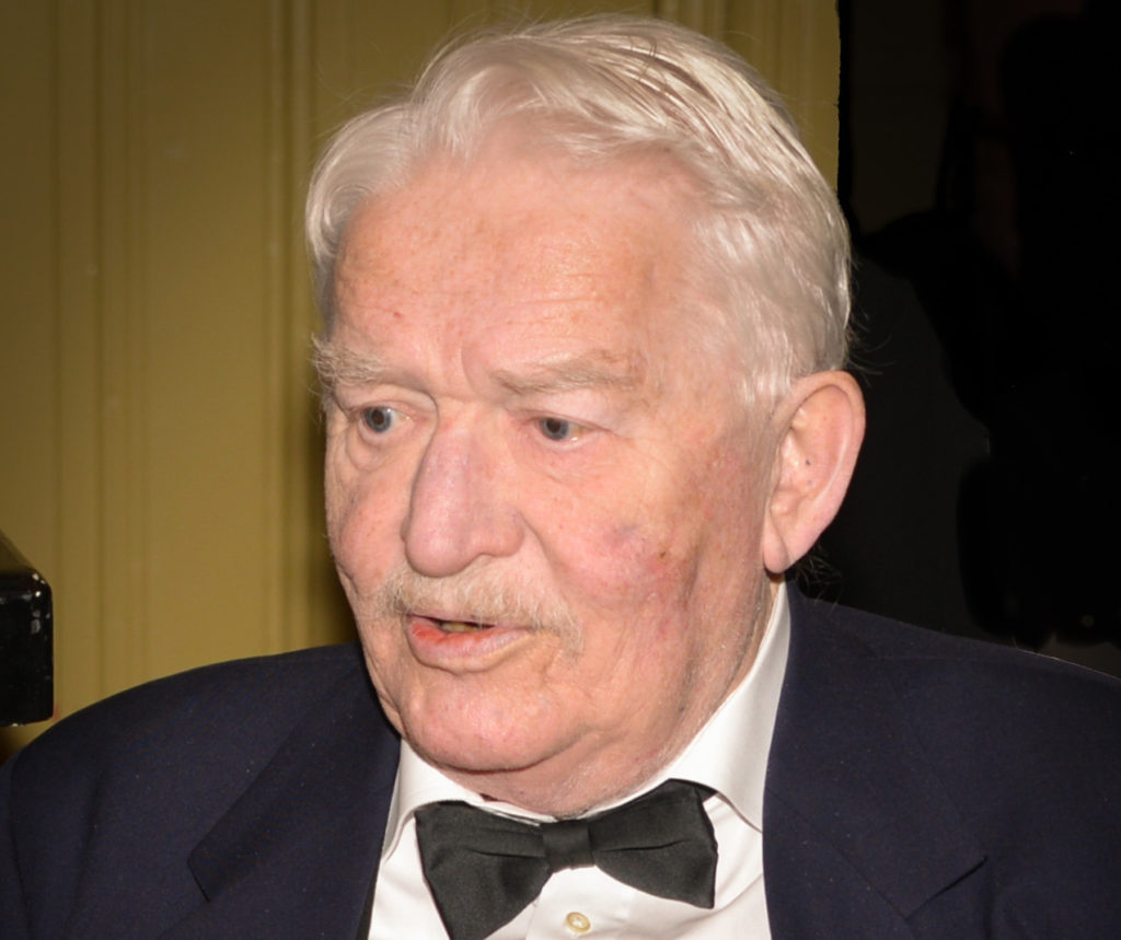 Hasse Alfredson. Han är ganska gammal och har vitt hår. Han har kostym och fluga på sig.