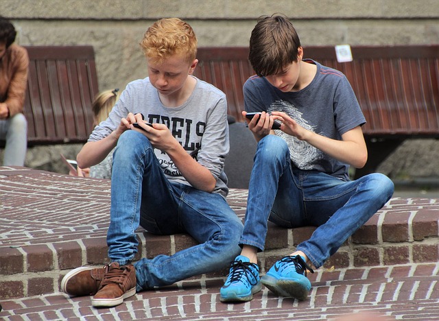 Två barn sitter med sina smartphones på marken.