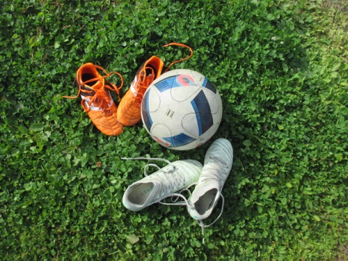 Närbild på en fotboll och fyra fotbollsskor på en grön gräsmatta.