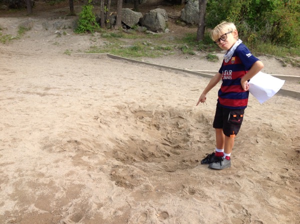 Ett barn pekar ner i en grop i sanden där bilen brukade stå.