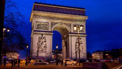 Triumfbågen är upplyst på kvällen. Det är en stor båge av sten, med statyer på sidorna.