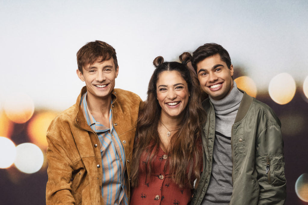 De tre programledarna står och håller om varandra och skrattar.