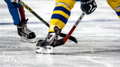 Två ishockeyspelare står på isen och tekar. Bara deras ben syns. Den ena har Sveriges färger på kläderna.