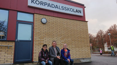 Annica, Mumen och Noah sitter på en bänk vid Korpadalsskolan.