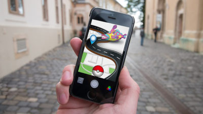 En mobiltelefon med Pokémon go i förgrunden och en gata i bakgrunden.