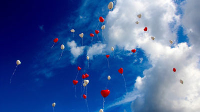 Hjärtformade ballonger som flyger upp bland molnen.