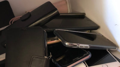 Foto på en hög med mobiltelefoner i ett skåp.