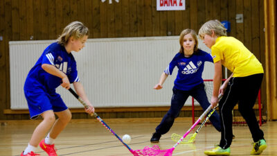 Tre barn som spelar innebandy.