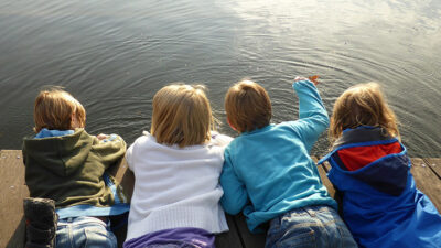 Fyra barn som ligger på mage på en brygga och tittar ner i vattnet.