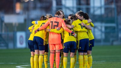 Fotbollsspelare som håller om varandra i en ring mitt p en fotbollsplan.